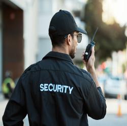 Person wearing a black security uniform holding a walkie talkie
