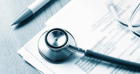 Close up of documents on a table with a pen and a stethoscope.