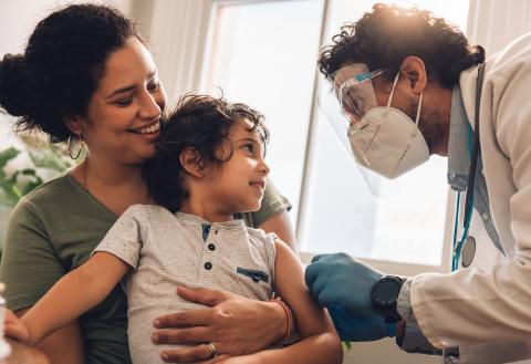 A child receives care from a pediatrician in a doctor's office as the caregiver holds the young child.