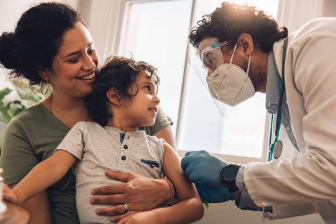 A child receives care from a pediatrician in a doctor's office as the caregiver holds the young child.