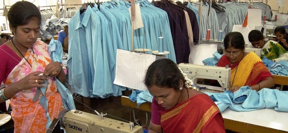 Women wearing red outfits sewing a blue garment on a white table