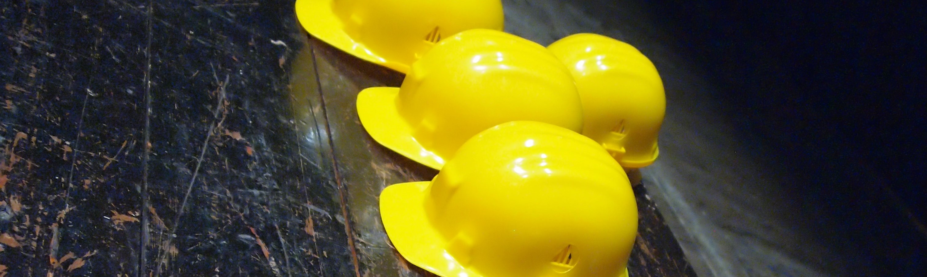 Five yellow hard hats on gray surface