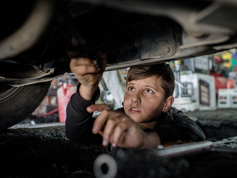 Boy with brown hair works on a car.