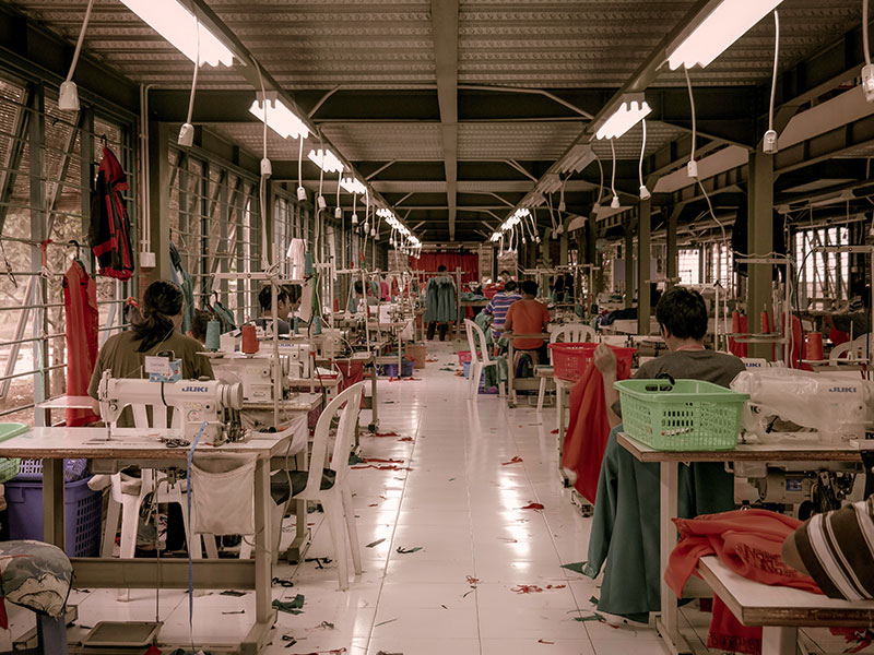 Women and men sewing in garment factory with white tile floors