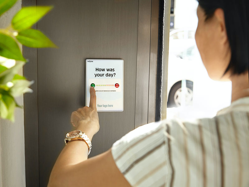Female employee pressing a green button to give feedback on a device at the company exit door.