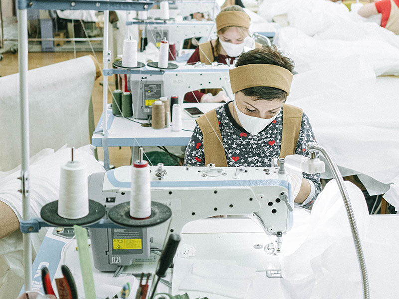 Women wearing white face masks working in a sewing/garment factory.