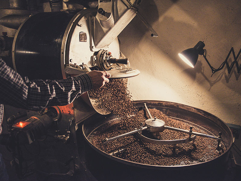 Person pouring coffee beans in a grinding machine.