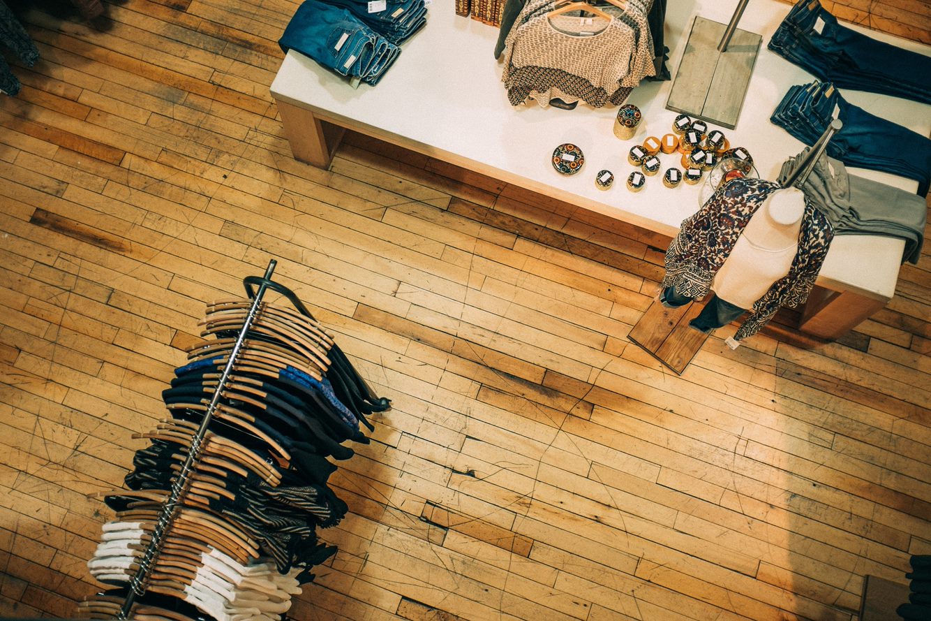 Various clothes in a shop with wooden floors. Jeans/Blouses/Shirts