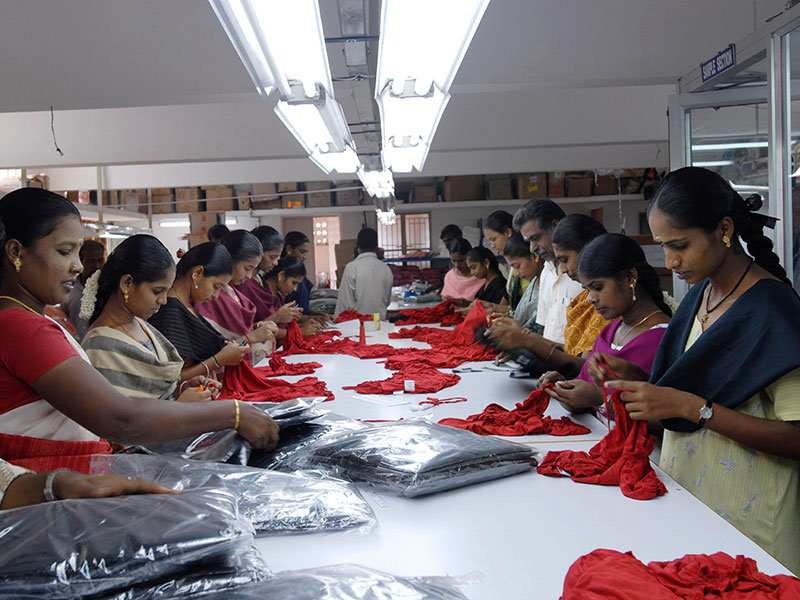 Women in red, green, and blue attire working at a table making red garments
