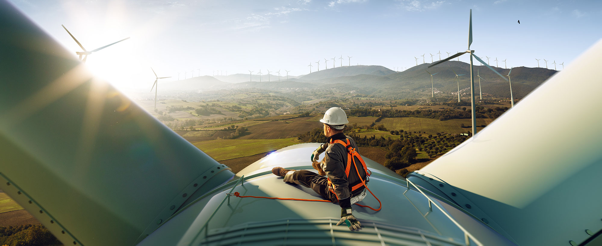 An engineer sitting atop a wind turbine looking out over the sunset.