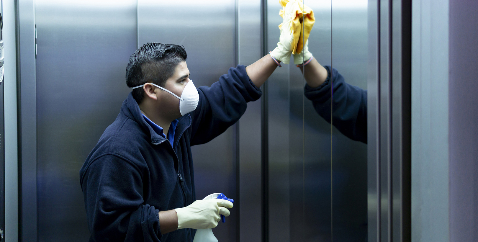 Janitor: A janitor cleaning a mirror in an elevator