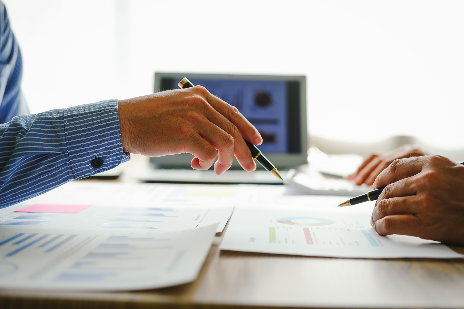 Two people reviewing printed charts and graphs at a table, pointing with pens during a discussion.