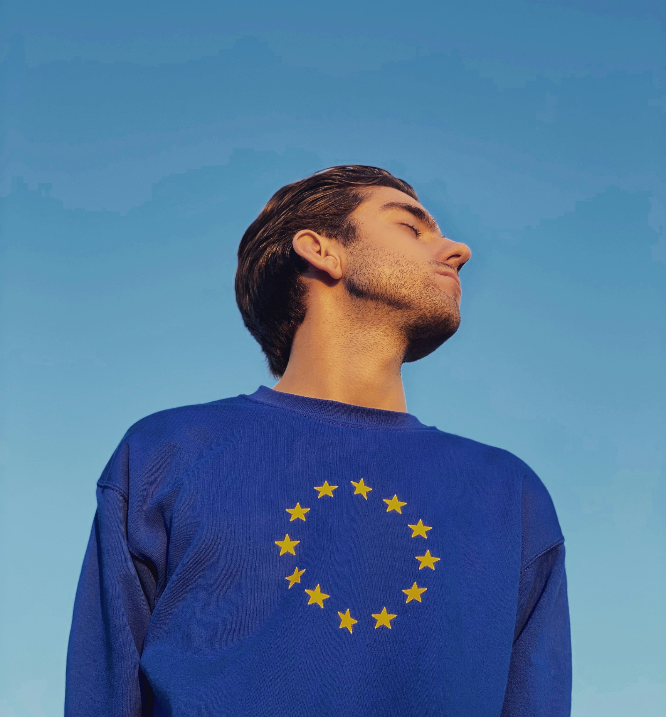 Man with brown hair wears a blue shirt with the European Union stars