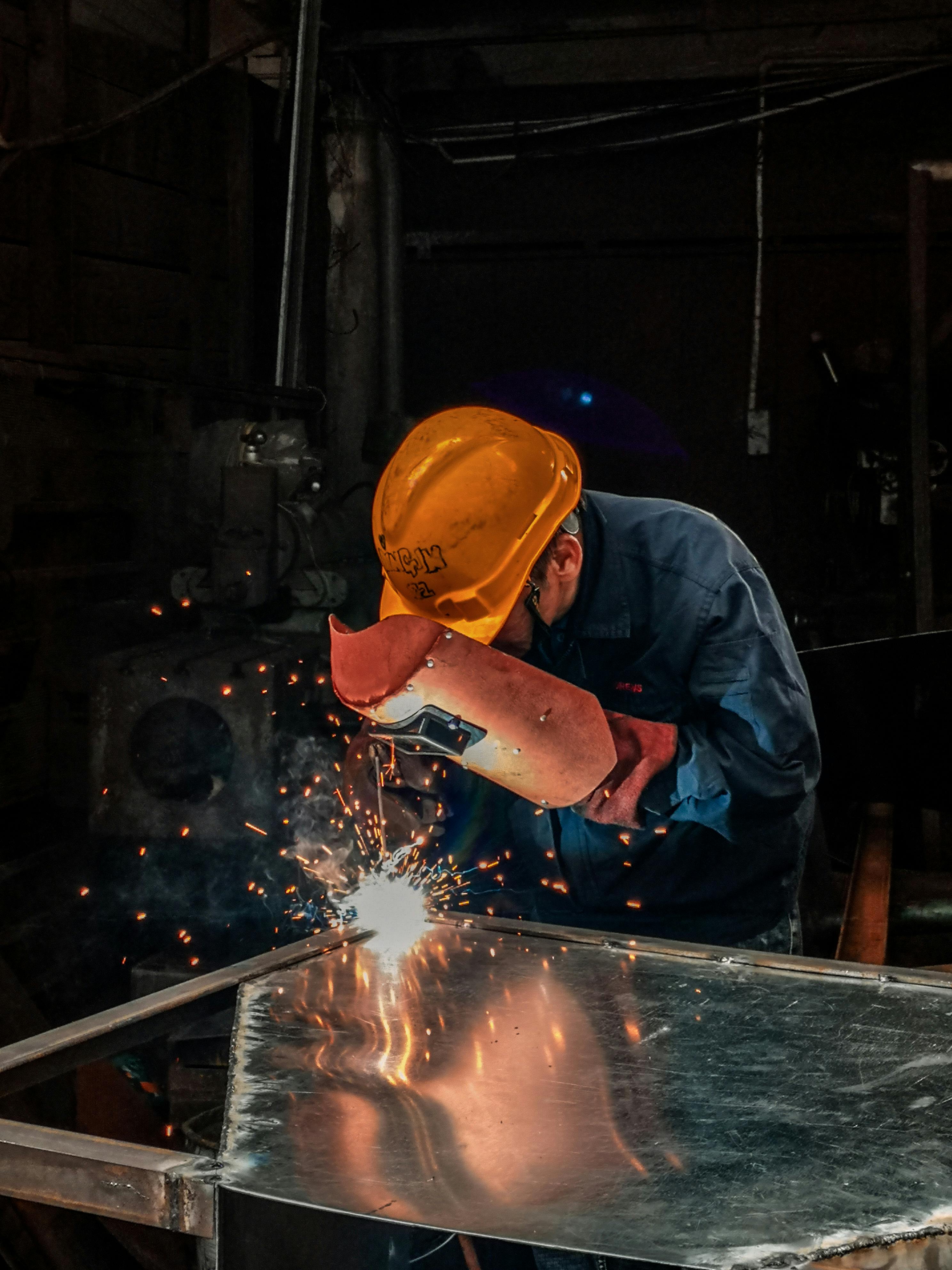 Man in orange hard hat holding a red welding mask and welding
