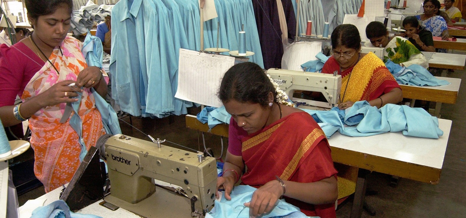 Women working at white tables working with blue fabric to make garments