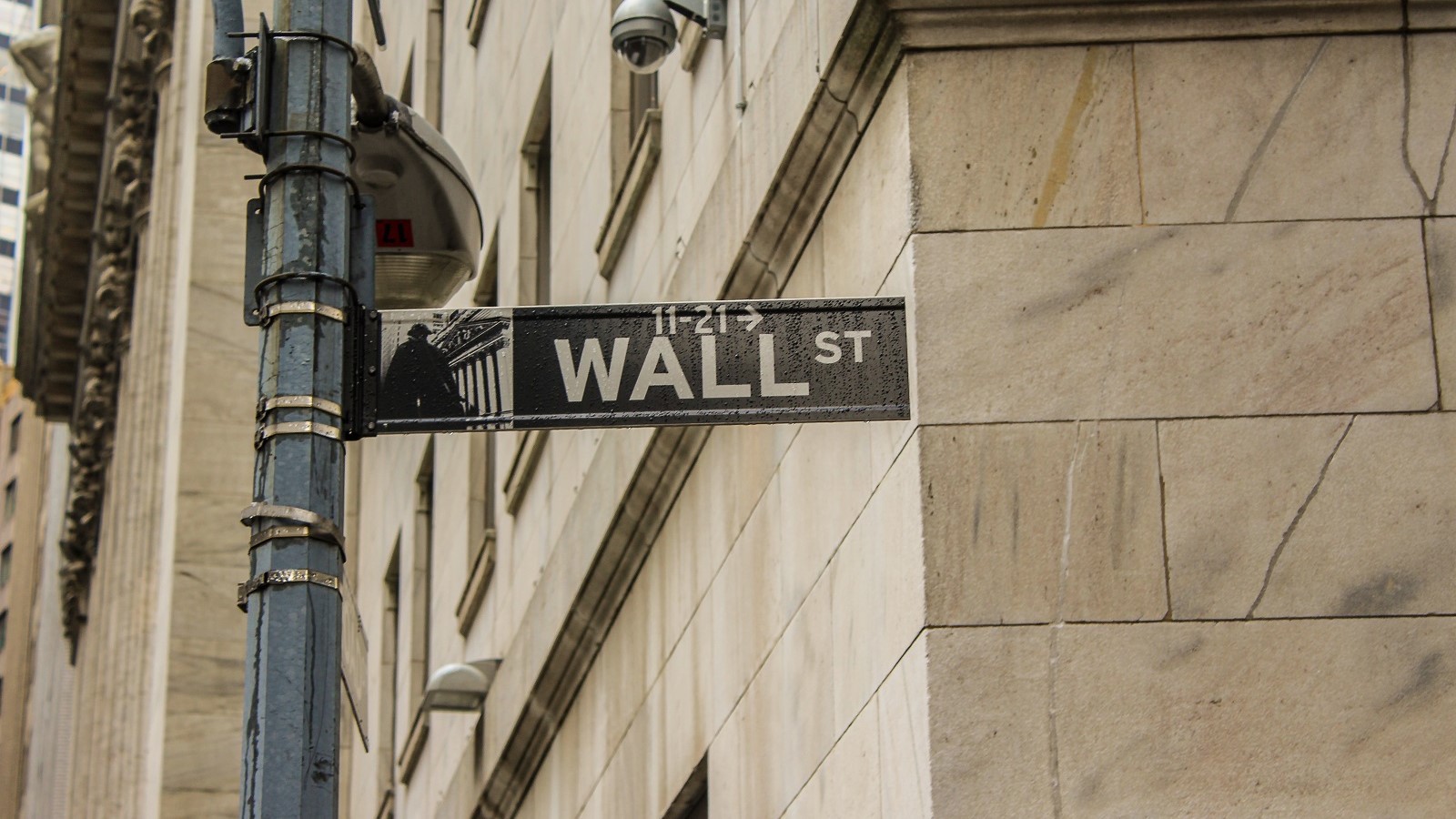 Street sign of Wall Street on a pole by a tan stone building