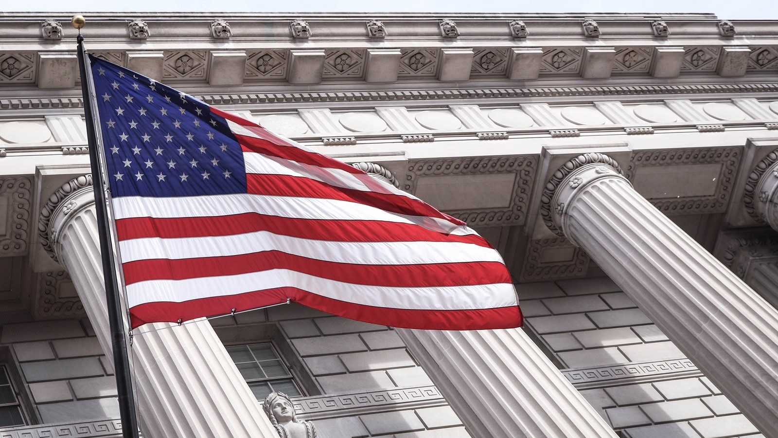 US flag flying on a pole by a white building with columns