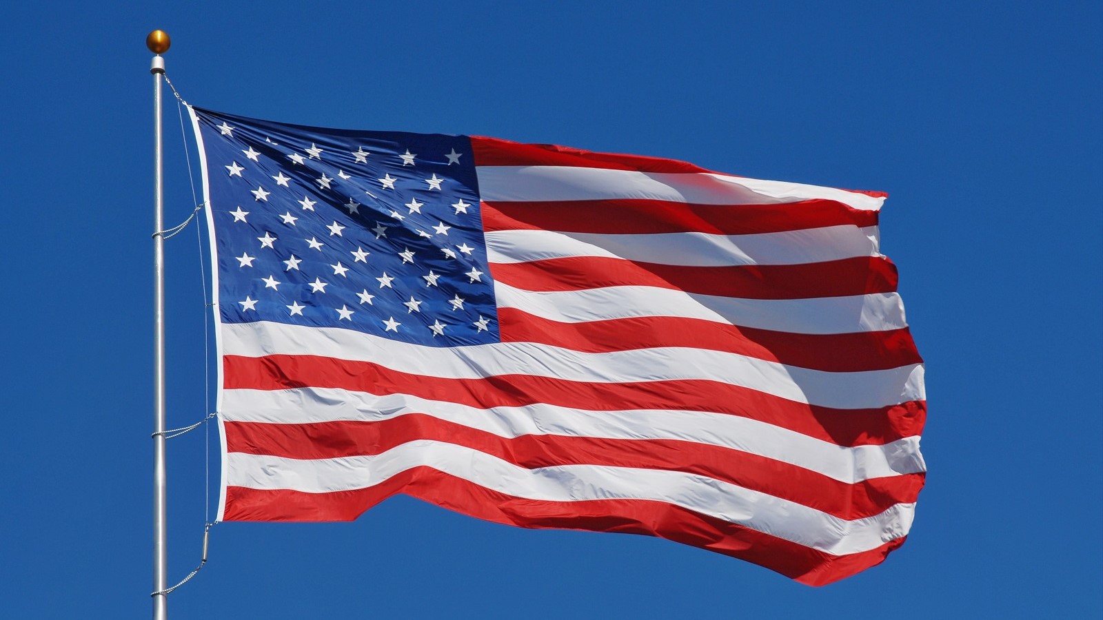 American flag on a pole blowing in the wind against a blue sky