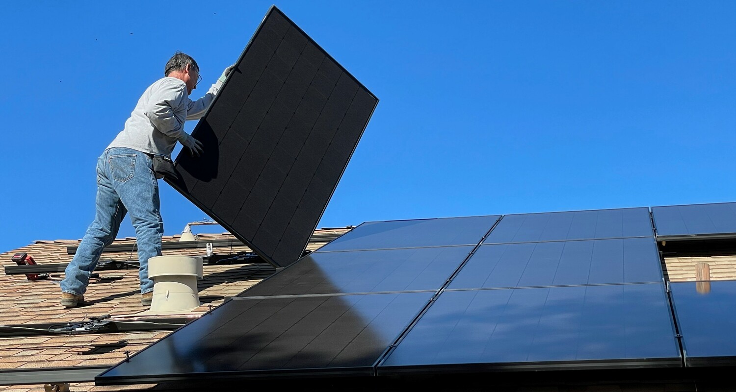 An engineer installs a solar panel on the roof of a residential home.