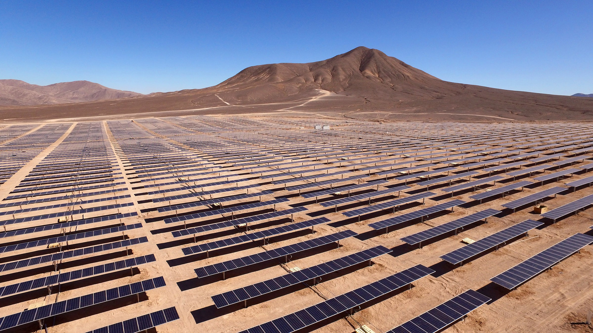 An expansive field of solar panels in the desert with a mountain in the background.