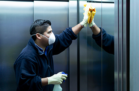 Masked worker sanitizing elevator