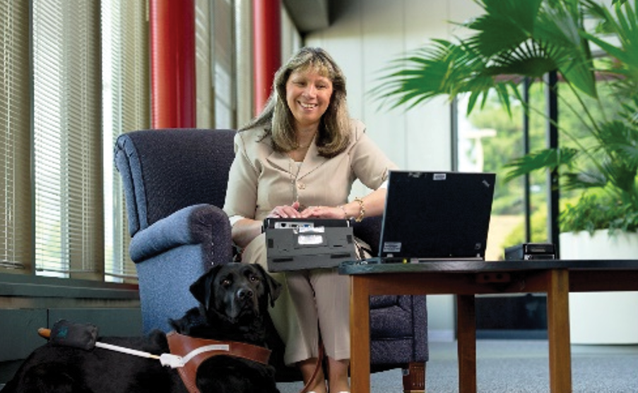 Smiling mature woman typing with a dog lying on the floor.