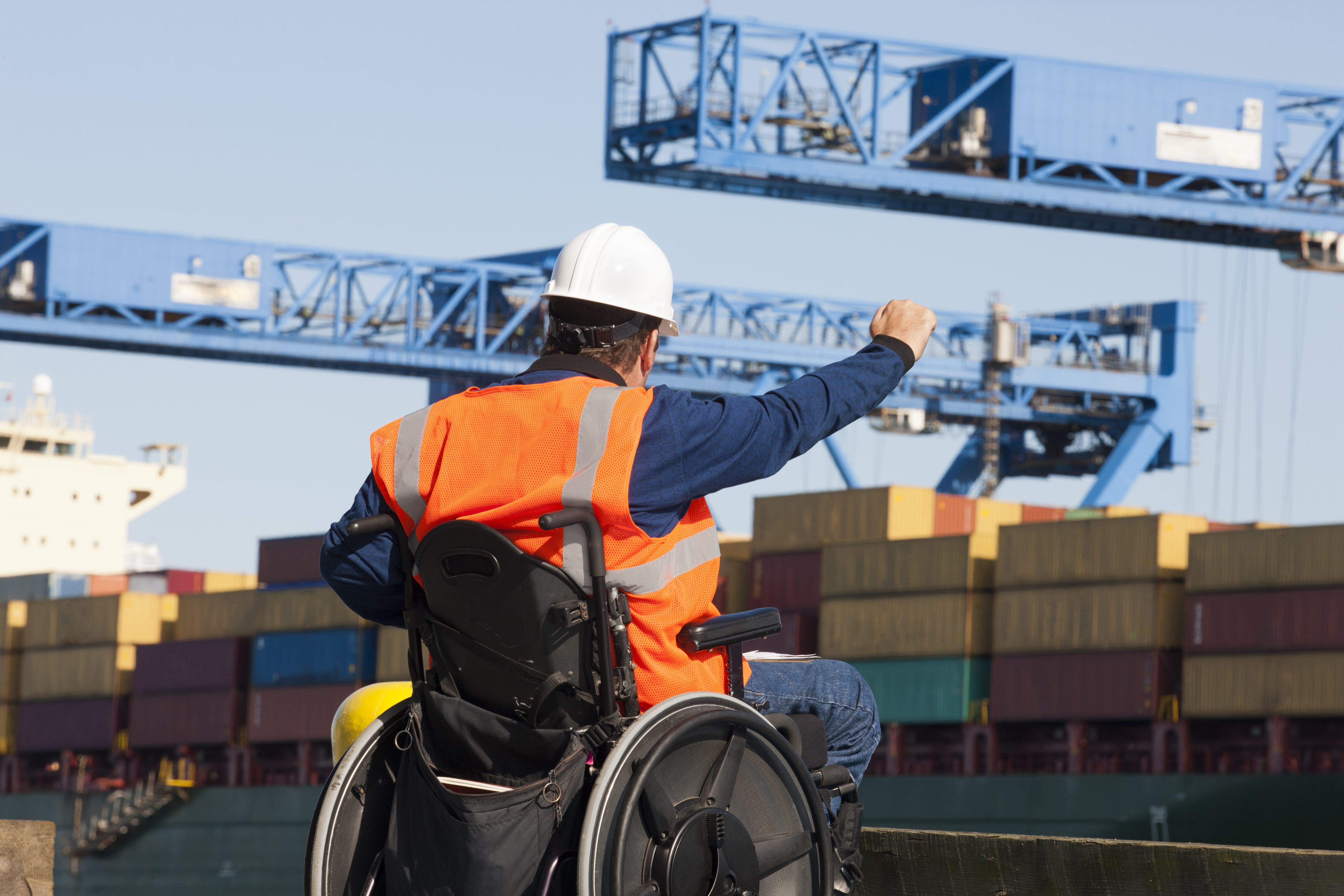 Transportation engineer worker and wheelchair user giving directions to shipping containers at shipping port.