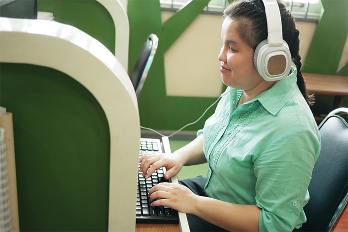 A blind person wears headphones and types at a computer keyboard
