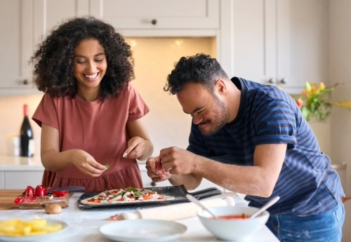 An aide helps a person with Down syndrome assemble a pizza to bake in a cozy home kitchen.