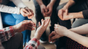 Close-up photo of a small support circle containing five people, focusing on their hands. 