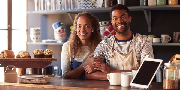 A smiling couple stands behind the counter of a caf.