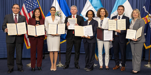 Deputy Secretary Julie Su poses with government representatives from El Salvador, Guatemala and Honduras in front of flags from all four countries. 