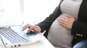 A pregnant woman works at a laptop. 
