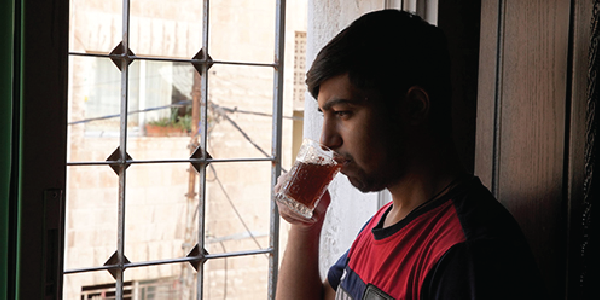 Yousef sips from a glass cup in front of a window.