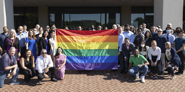 Department staff pose in front of the Frances Perkins Building holding the Pride flag.