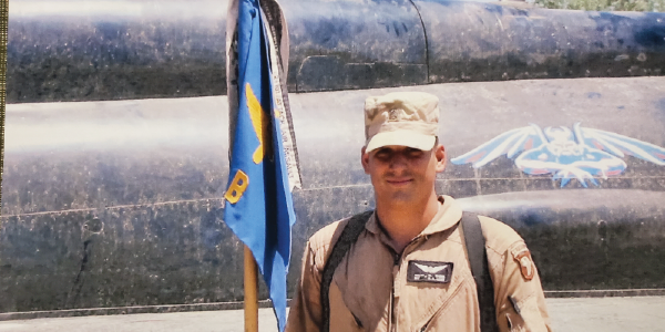 Smiling veteran holds unit flag. 