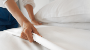The hands of a housekeeper smooth out crisp white bedsheets on a hotel bed.