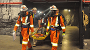 Mine rescue workers in protective suits and helmets carry a stretcher in a mine rescue simulation.