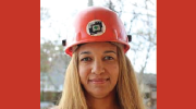 A woman in a hardhat smiles at the camera.
