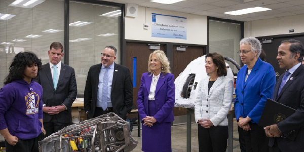 A student displays a rudimentary robot to several adults, including Secretary Walsh and First Lady Jill Biden.