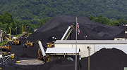 Wide-shot view of a coal mine, with coal stacked high above the building roofs and several large vehicles moving material around the site.