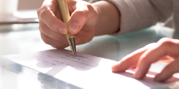 Close-up shot of a person signing a check with a gold pen.