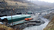 The entrance to the Sago coal mine. A conveyor belt rises up a hill and water pools at the hill’s base. Bare winter trees stretch toward an overcast sky.