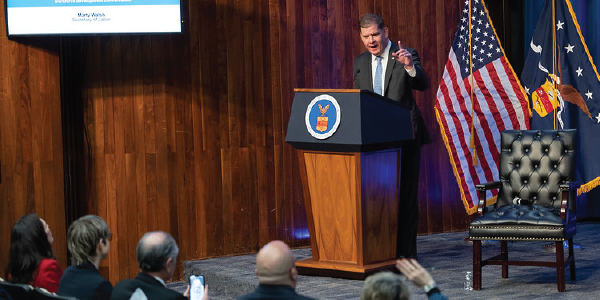 Secretary Walsh stands at a podium bearing the department seal, addressing a crowd. 
