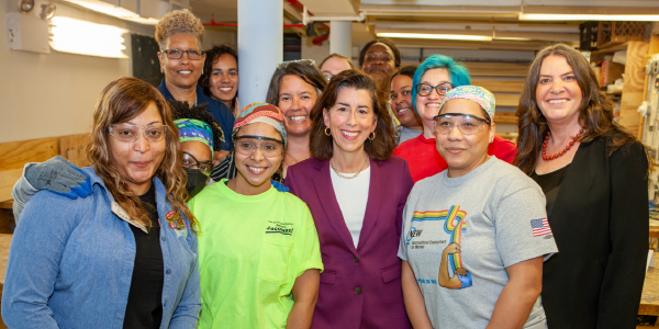 Wendy Chun-Hoon and Gina Raimondo pose with 11 women some in protective goggles in a workshop.