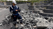 An MSHA inspector stands on crushed rock above a quarry, taking notes.