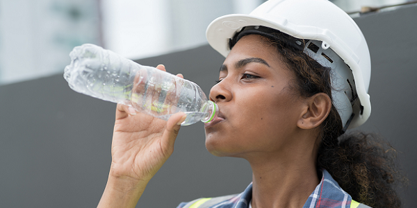 A female worker in a hard hat drinks from a water bottle.