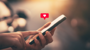 A person taps a cellphone. A heart icon appears above the phone.