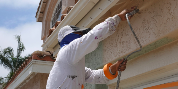 Image of a construction worker applying paint to the stucco on the exterior of a house.