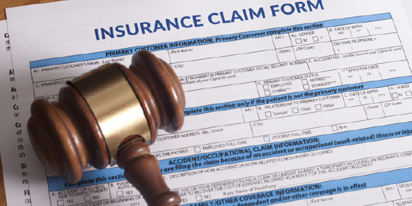 A judicial gavel lies on top of a stack of insurance claim forms.